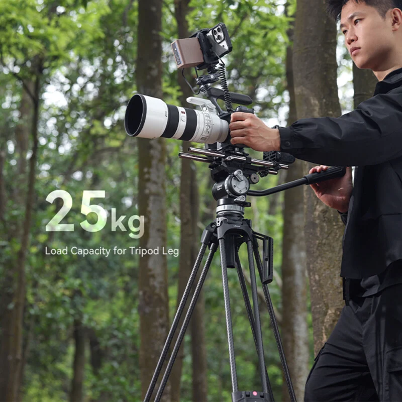 Man operating a camera mounted on a tripod with a load capacity of 25 kg in a wooded area.