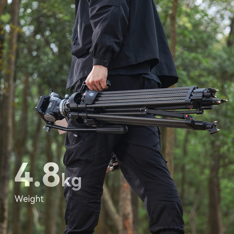 A person walking in a forest, carrying a large professional camera mounted on a tripod over their shoulder, with the text "4.8kg weight" displayed.