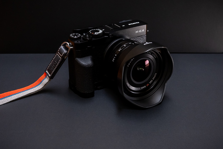 A fujifilm x-e4 mirrorless camera with a prime lens and a multicolored strap against a dark background.
