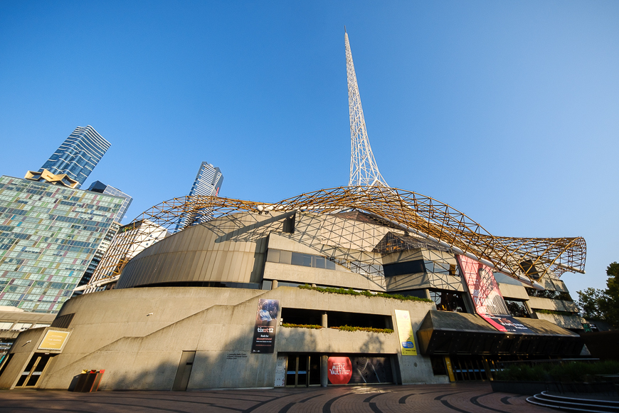 Modern arts center with distinctive spire and geometric framework under a clear sky.