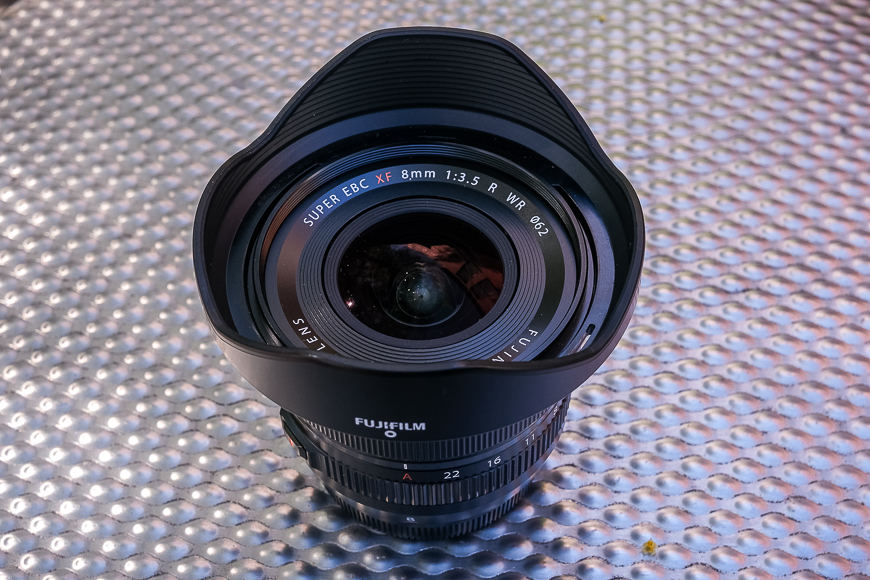 A fujifilm 8mm f/3.5 camera lens displayed on a textured surface.