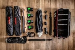 Photography equipment neatly arranged on a wooden floor, including lights, battery packs, stands, and a rolling case.