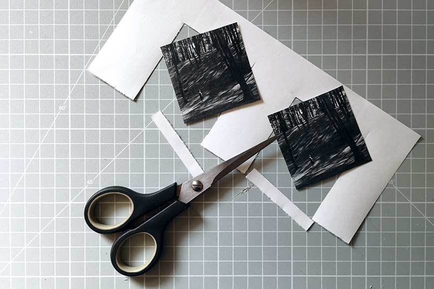 A pair of scissors on a cutting mat with pieces of paper, some scribbled with black marker.