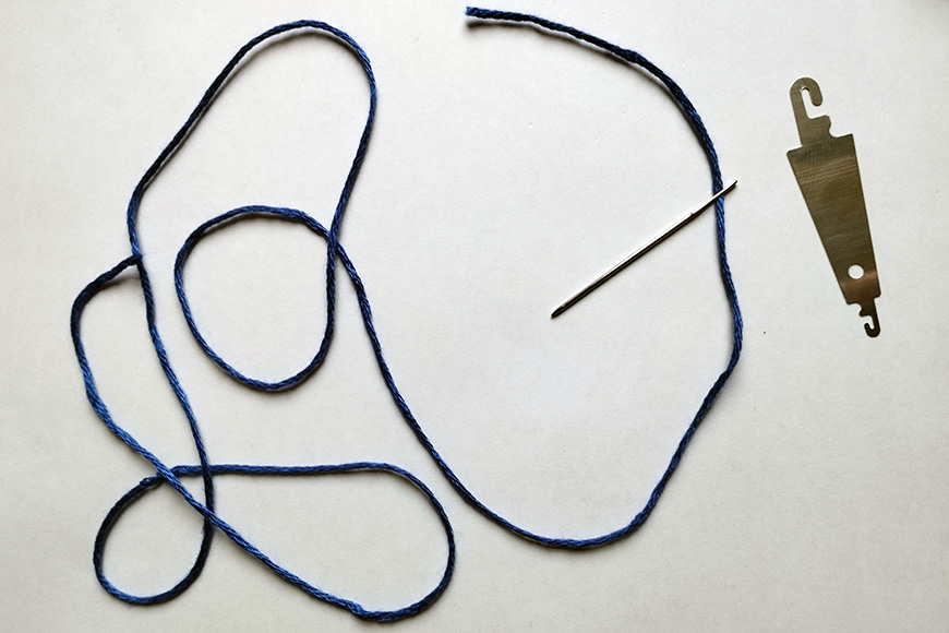 A blue string, a silver needle, and a brass-colored saw blade laid out on a white surface.