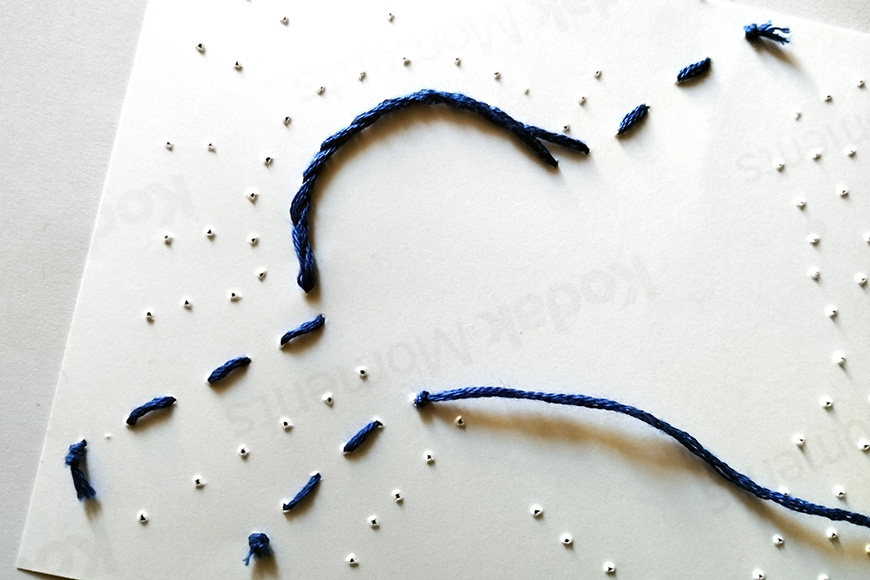 Close-up of a white paper with a blue thread partially threaded through small holes creating an abstract design.