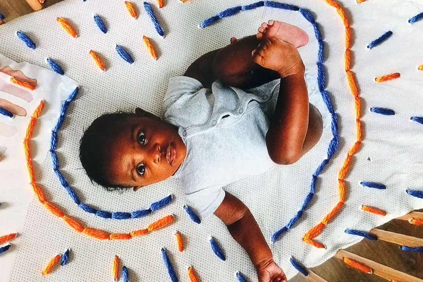 Baby lying on a circular play mat with colorful decorations, looking up at the camera.