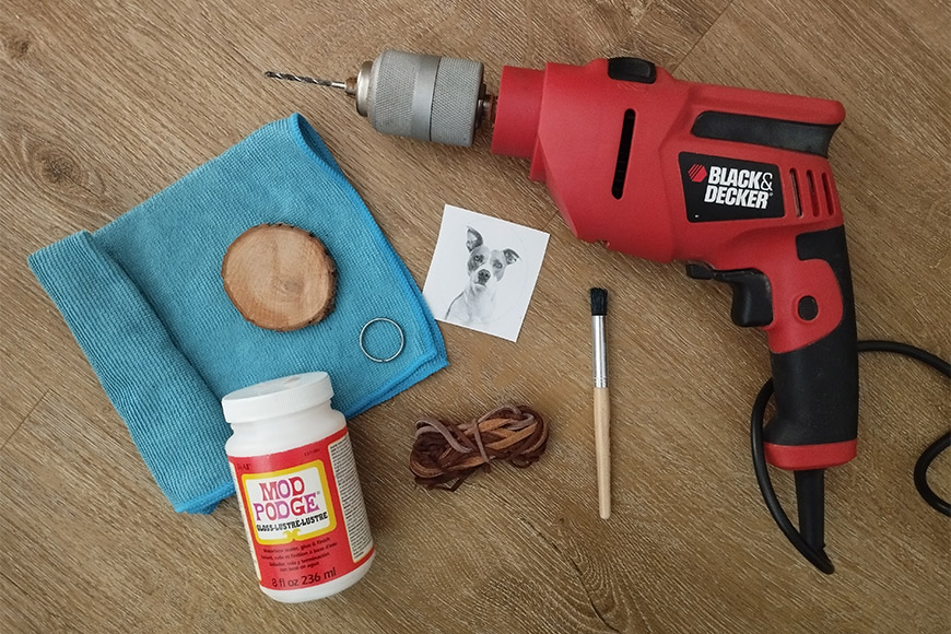 Red black & decker drill, blue cloth, wooden disk, photo, mod podge glue, brush, and brown strings on a wooden floor.