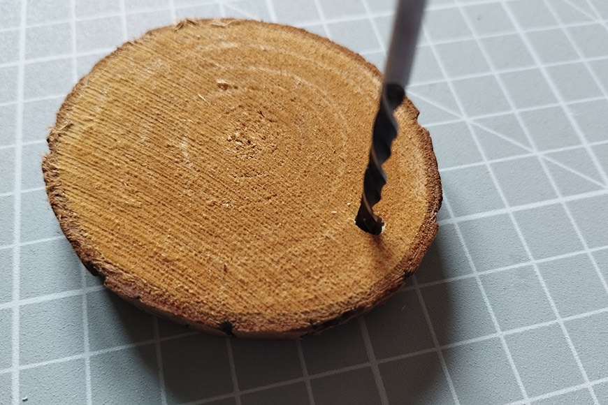 A close-up of a wooden disc with a drilled hole on a cutting mat.