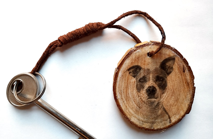 A wooden keychain featuring a laser-engraved image of a dog's face, attached to a metal key with a leather loop.
