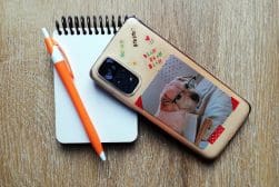Smartphone with a dog-themed case alongside a notepad and pen on a wooden surface.