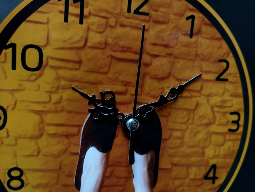 Close-up of a clock face with ornate hands, showing the time approximately 12:15, set against a textured yellow and black background.