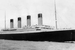 Black and white historical photo of the rms titanic at sea, showcasing its prominent four funnels and large hull.