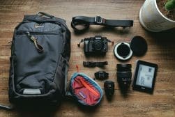 Photography equipment spread on a wooden floor, including a camera, several lenses, a backpack, and a tablet.