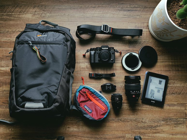 Photography equipment spread on a wooden floor, including a camera, several lenses, a backpack, and a tablet.