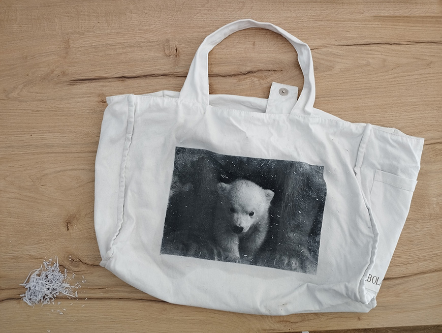 A white canvas tote bag with a black-and-white image of a bear on it, lying on a wooden surface.