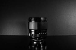 A camera lens positioned centrally against a dark background with a reflective surface.