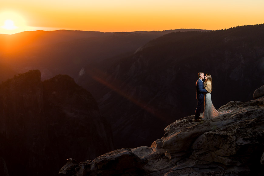 A couple embraces at sunset on a mountain overlook.