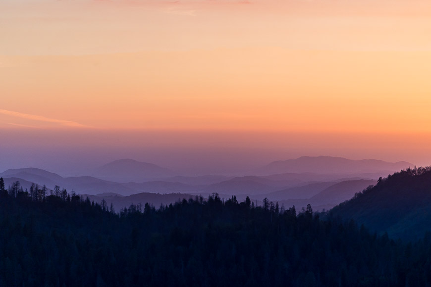 Sunset over layered mountain silhouettes with a gradient sky.