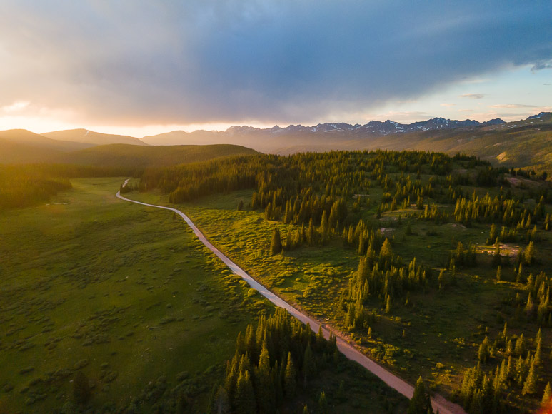 Aerial view of a winding road through a forested landscape at sunset.