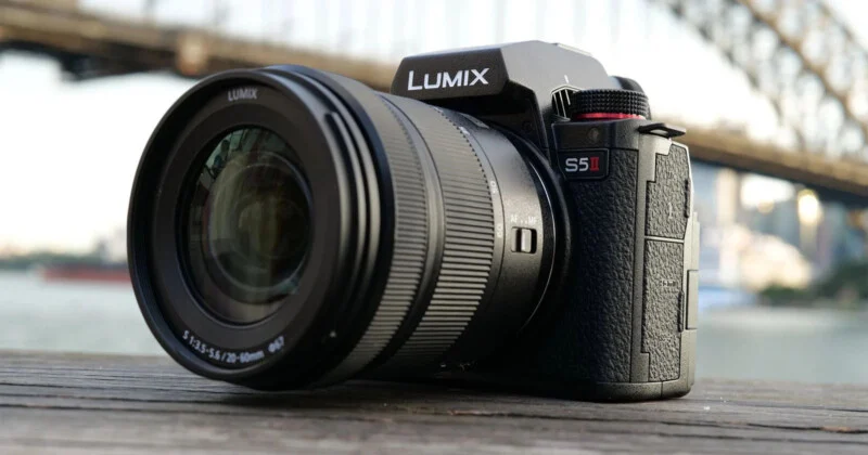 A lumix s5 mirrorless camera placed on a wooden surface with a bridge in the background.