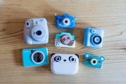A collection of six colorful instant cameras, designed with playful elements, arranged on a wooden surface.
