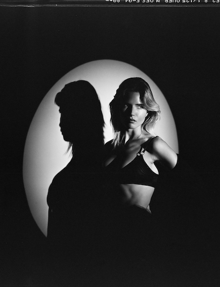 Black and white portrait of a woman with a shadow profile silhouette against an illuminated backdrop.