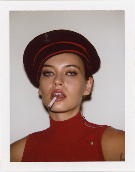 Woman wearing a red beret and sleeveless top, with a cigarette in her mouth.