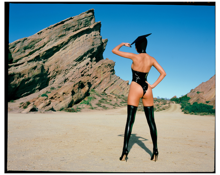 Model in black outfit and high heels posing in a desert landscape.