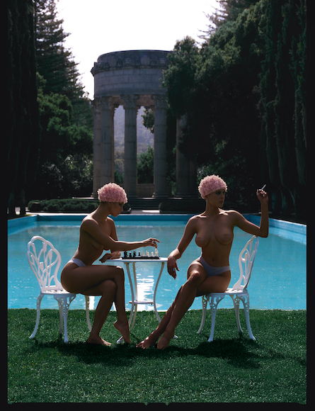 Two individuals with swim caps seated by a pool, one playing chess.