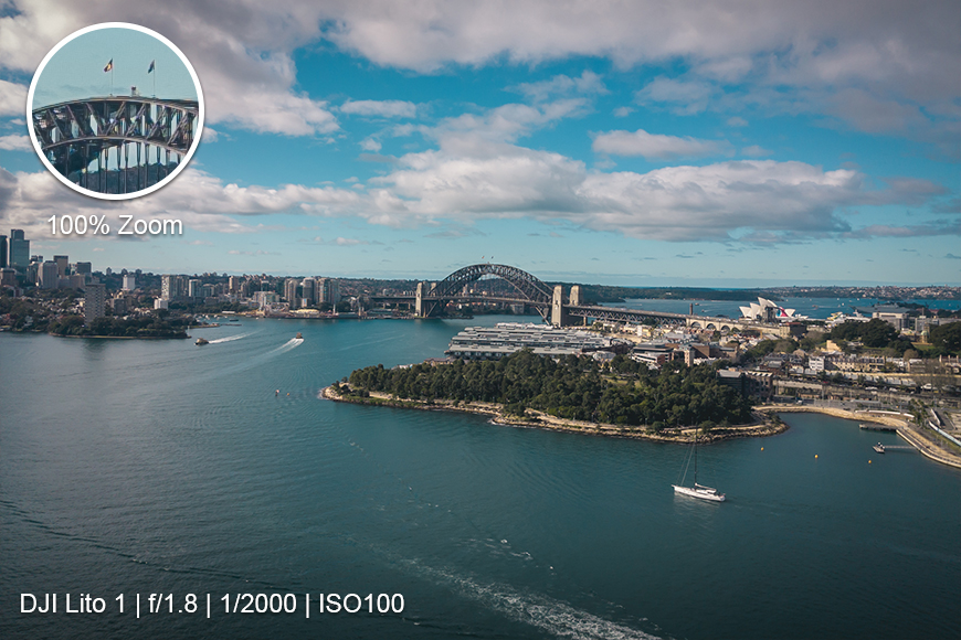 Aerial view of Sydney Harbour with the Harbour Bridge and Opera House; zoomed inset shows bridge detail. Camera settings displayed at bottom left.