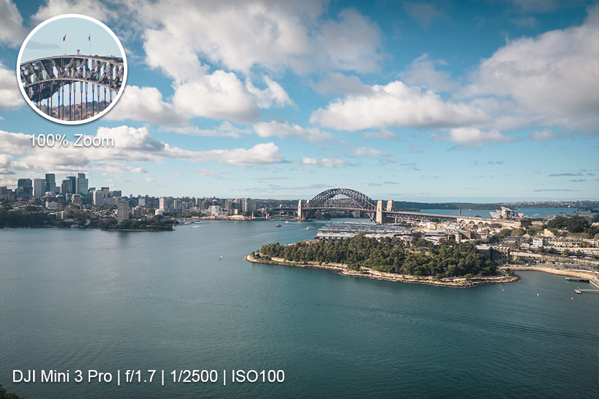 Aerial view of Sydney Harbour with the Sydney Harbour Bridge and city skyline; circle inset shows bridge details at 100% zoom. Camera settings are displayed at the bottom.