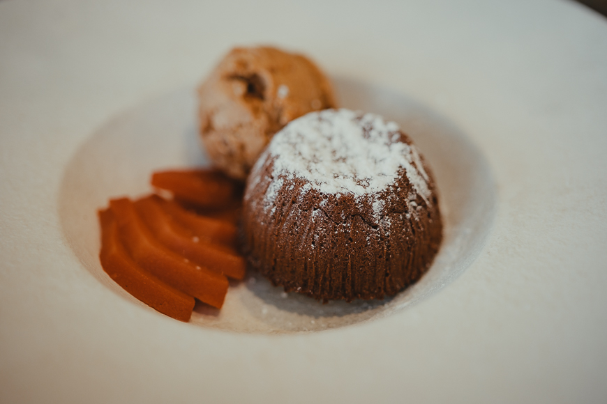 Chocolate lava cake dusted with powdered sugar, served with a scoop of ice cream and thin slices of poached pear on a white plate.