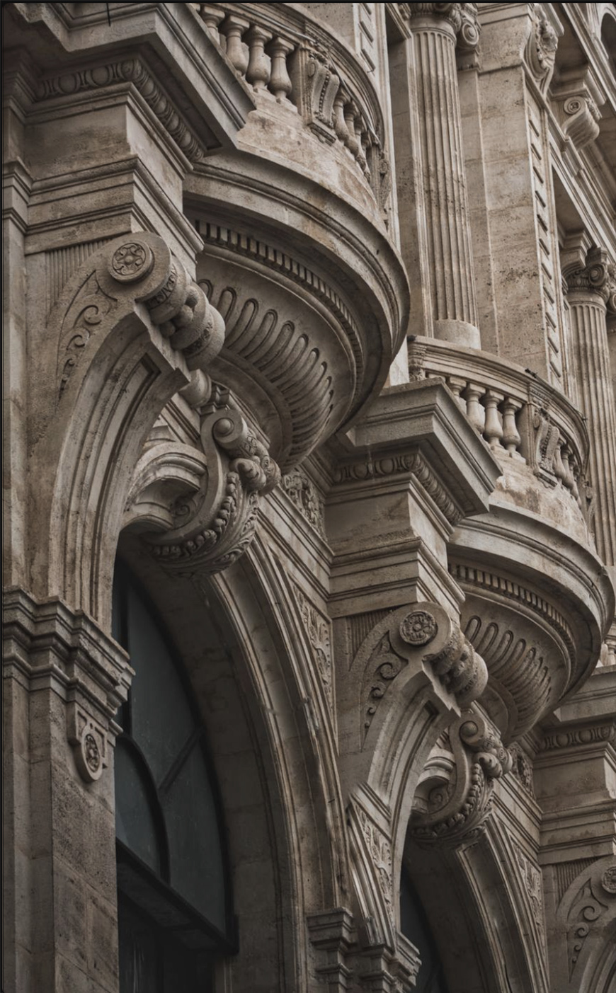 Close-up view of ornate stone arches and columns on a classical building facade, featuring intricate carvings and decorative architectural details.