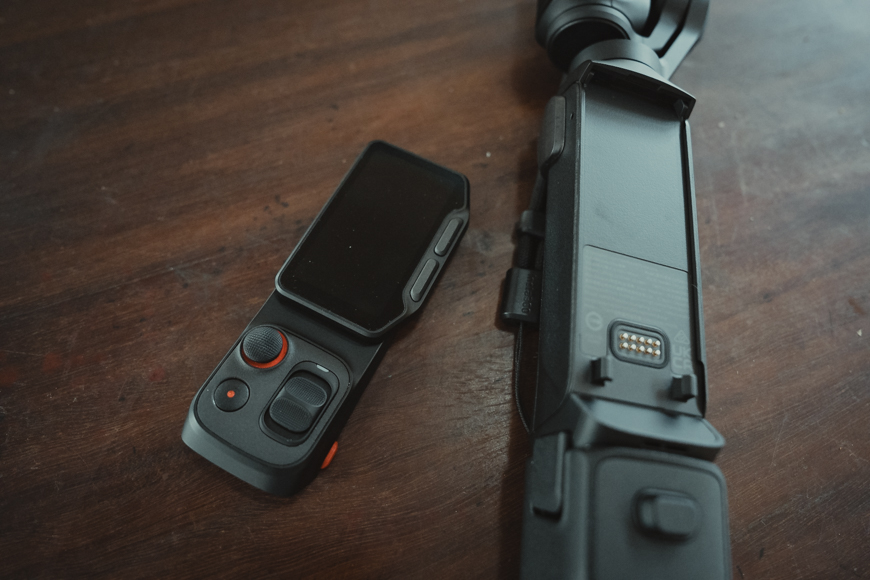 A handheld camera gimbal with a touchscreen controller is placed on a wooden surface.