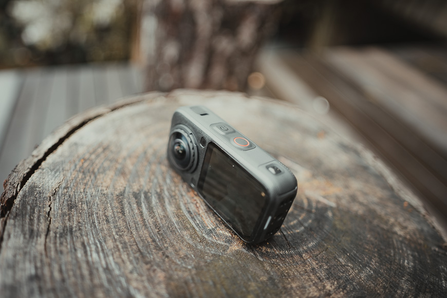 A black 360-degree action camera resting on a wooden stump.