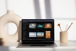 A laptop displaying a photo editing program, Luminar 2026 interface, sits on a white desk with a decorative vase and a cup holding paintbrushes.