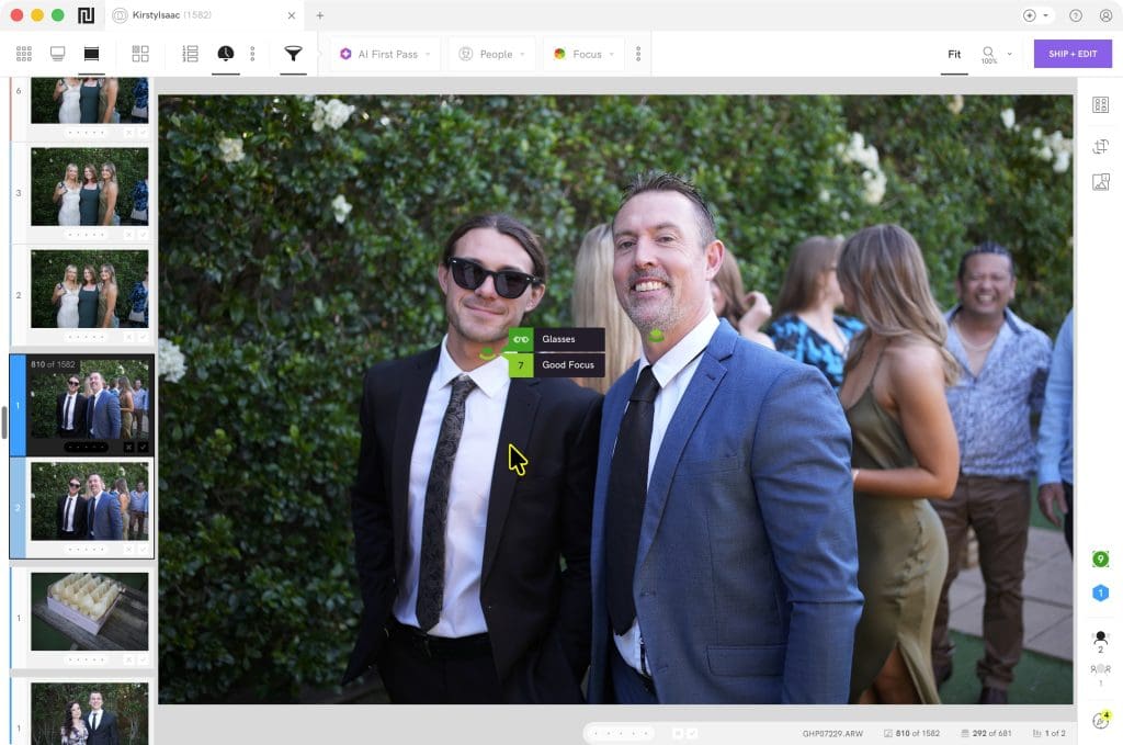 Two men in suits smile at the camera at an outdoor event, with other people and greenery in the background.