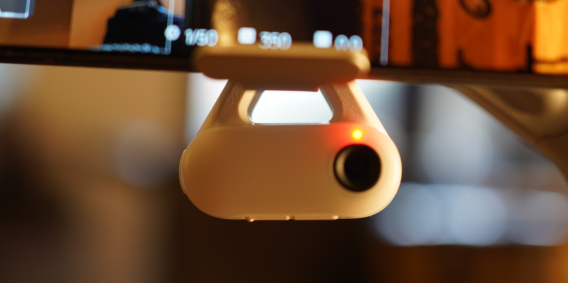 Small white camera device mounted to a screen, displaying a glowing red status light.