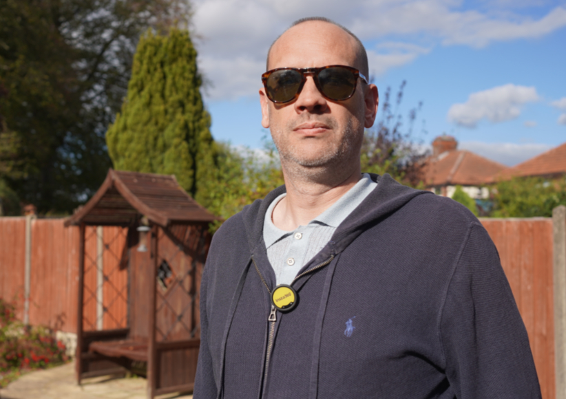 A man wearing sunglasses and a zipped hoodie with a small circular tag attached to the zipper.