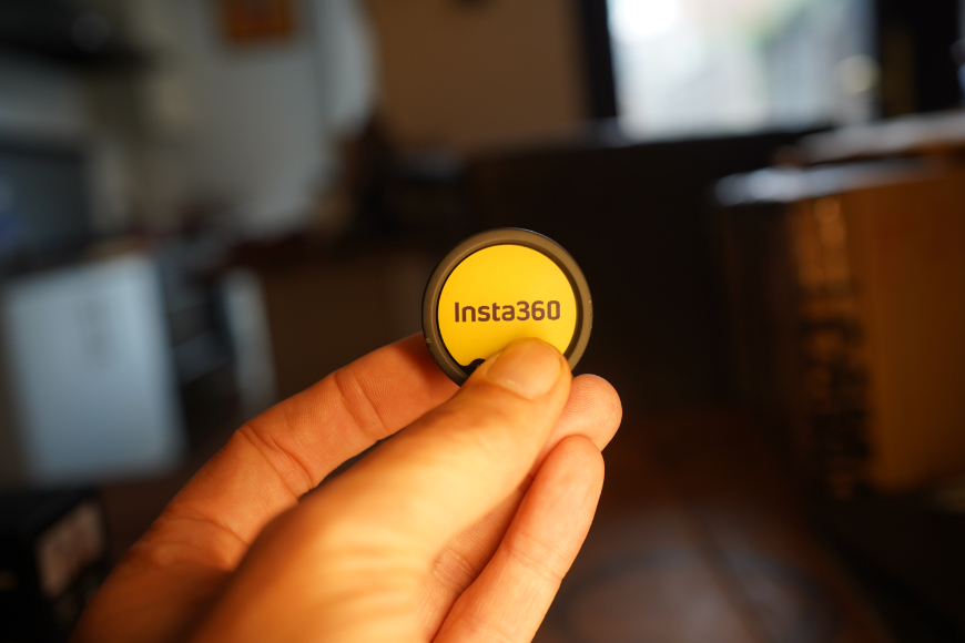 A hand holds a circular yellow disc labeled “Insta360.”
