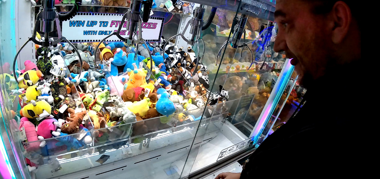A man looks into a claw machine filled with assorted plush toys.