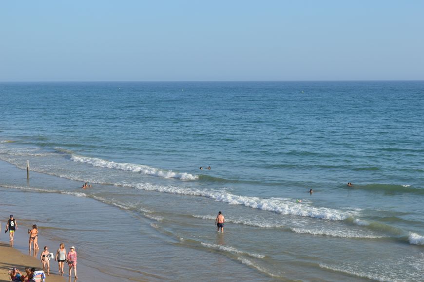 People walking along the shore and wading into the ocean on a sunny day.