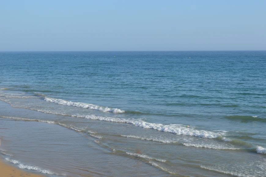 View of the ocean from above, showing gentle waves rolling onto the sandy shore.