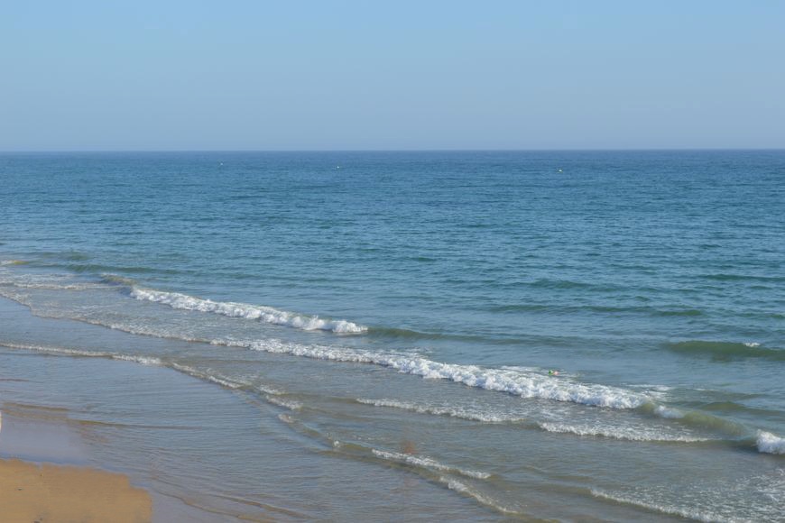 Ocean waves washing onto a sandy beach under a clear sky.