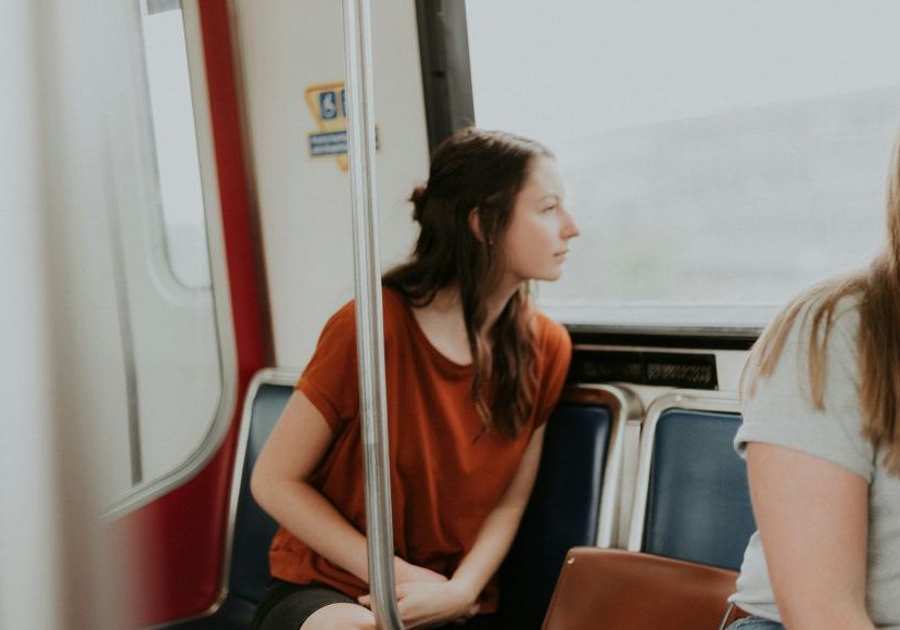 Two women sitting on a train looking at each other.