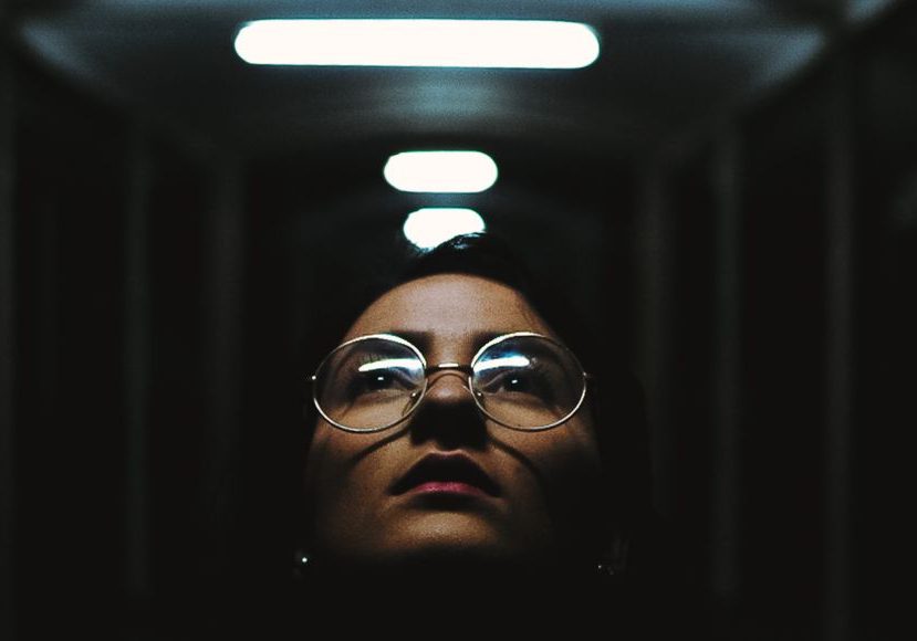 A woman in glasses standing in a dark hallway.