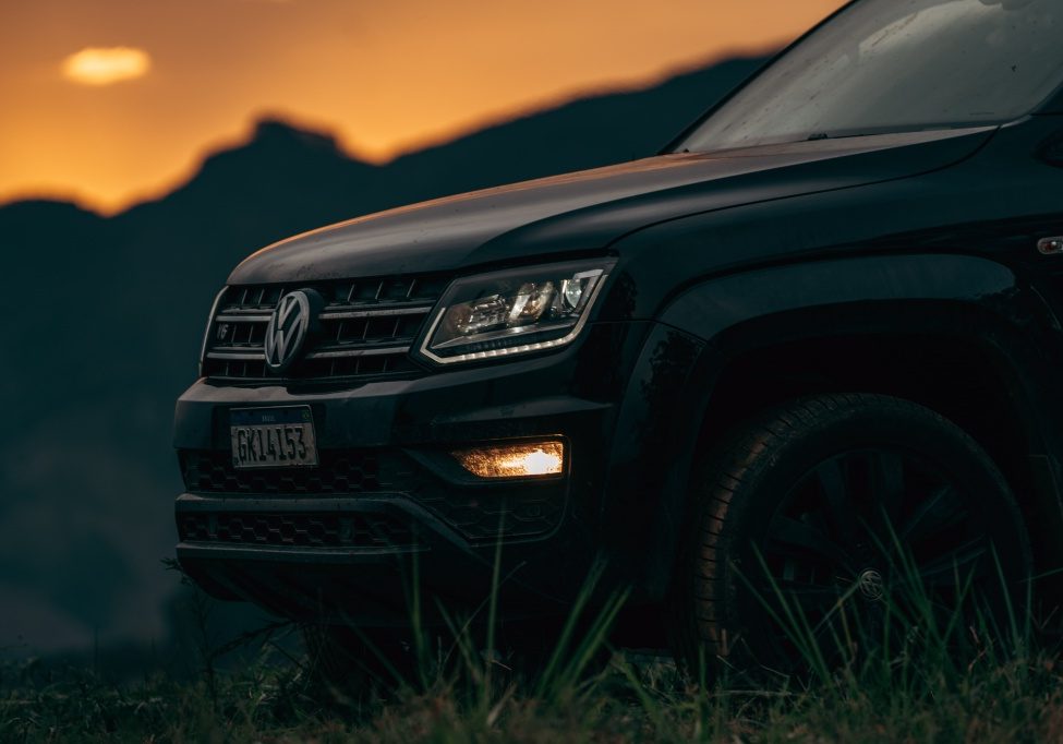 A black volkswagen atlas parked in a grassy field at sunset.