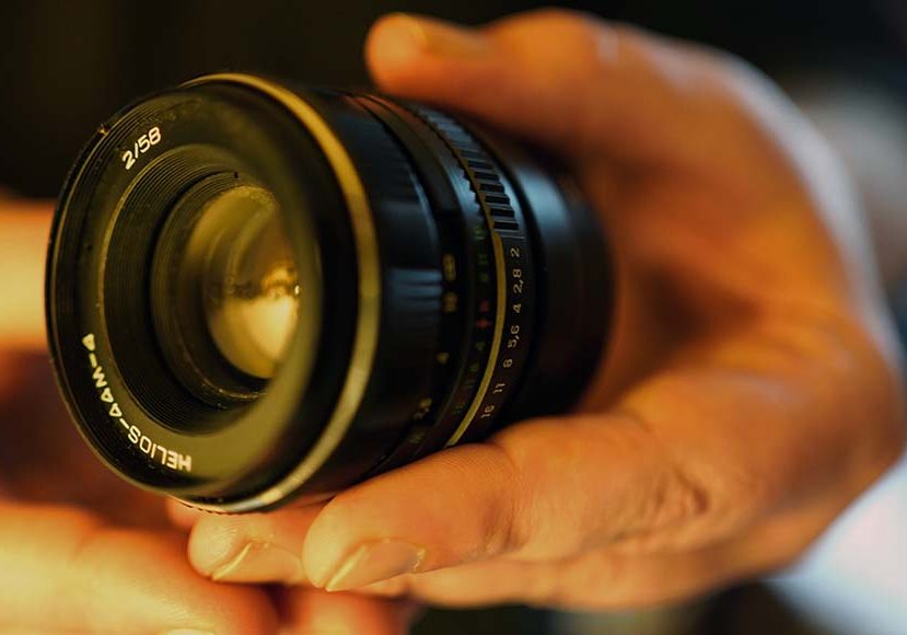 A person's hand holding a camera lens.