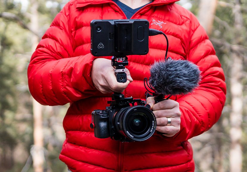 Person in a red jacket holding a camera rig with a smartphone and external microphone.
