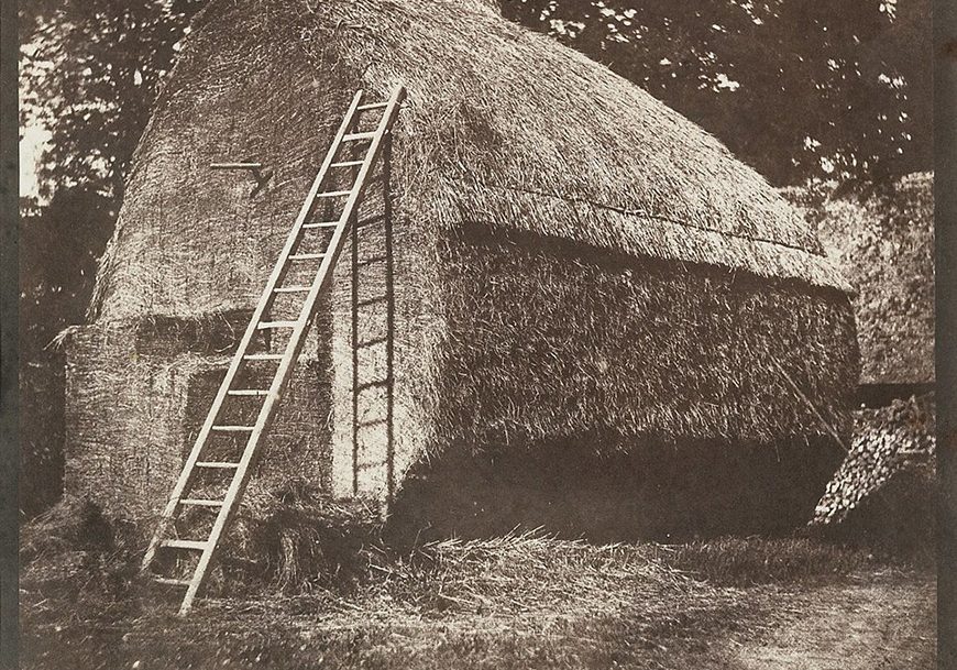 an old photo of a thatched house with a ladder.